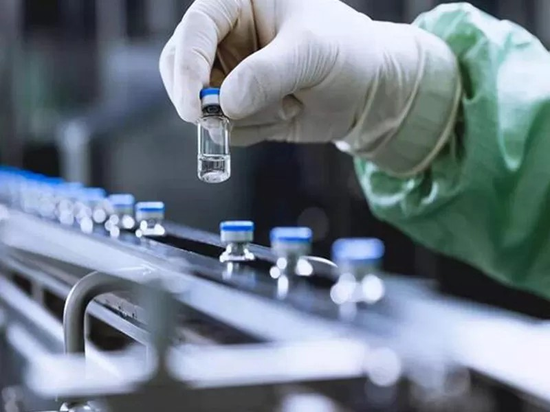 A gloved technician inspects a clear liquid sample during quality control testing.